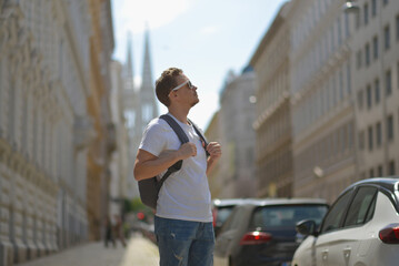 A man wearing white sunglasses and gray backpack on the street in Vienna on a hot sunny summer day. Tourism and sightseeing concept