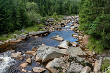 Serene mountain stream meandering through a lush forest, with large rocks and boulders scattered throughout the clear flowing water. High quality photo