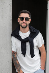 Fashionable handsome hipster man with sunglasses in a white T-shirt with a sweater on his shoulders...