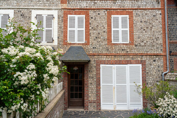 An empty yard of a classic stone house with closed shutters and flowering bushes. The concept of a quiet peaceful life in Western Europe.