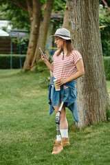 A young woman with a prosthetic leg enjoys a sunny day in the park, checking her phone while holding a cup of coffee.