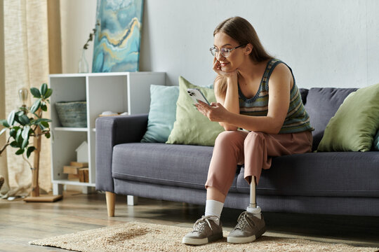 A young woman with a prosthetic leg relaxes on a couch in her living room, looking at her phone.