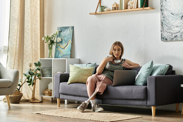 Obraz premium A young woman with a prosthetic leg sits on a couch in her modern living room, using a laptop.
