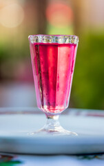 A glass of pink liquid is sitting on a white plate