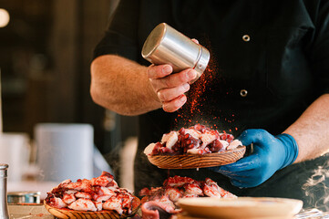 Unrecognizable kitchen professional pouring paprika on a plate of Galician octopus. Cook preparing tapas. Traditional food from the north of Spain