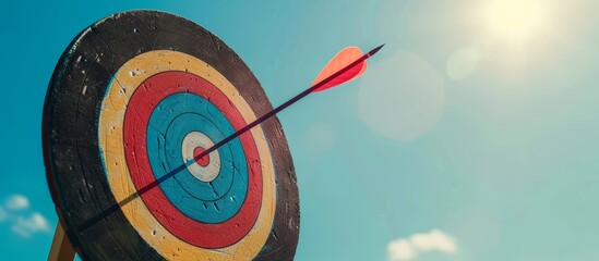 Closeup of target board or dartboard with arrow in the center of the board against bright blue sky. Business sucess, determination, goal, and targeting concept