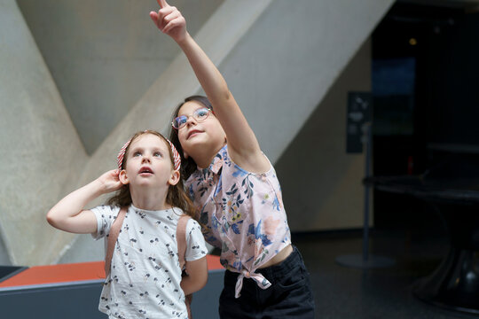 Two cute beautiful schoolgirls look up with surprise and interest in the museum. Children's education concept