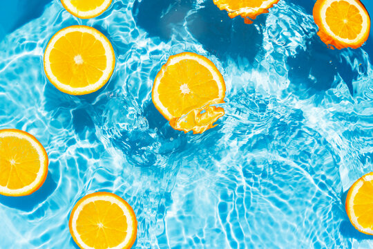 Creative summer composition made of sliced orange in transparent pool water. Refreshment concept. Healthy refreshing drink theme. Top view