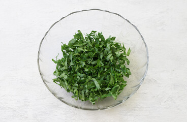 Chopped kale cabbage leaves, crushed with salt in a transparent bowl on a light gray background. Healthy detox food