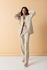 A young woman in a beige suit stands confidently against a pale background.