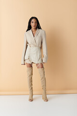 A young woman in a beige blazer and skirt poses confidently against a pale background, her long...