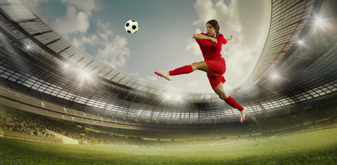 Female soccer player in red performs high jump kick on stadium field. Arena packed with spectators, and bright spotlights illuminate scene. Concept of sport, championship, team game, tournament. Ad