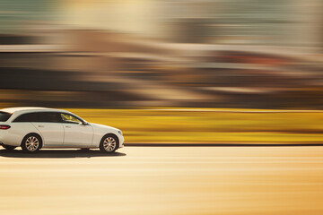 Fototapeta premium A white car is driving on an asphalt street on a sunny day with a blurred background at speed