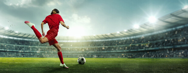 Female soccer player in red kicks ball on stadium field. Arena filled with enthusiasts, and field brightly lit with sunlight and spotlights. Concept of sport, championship, team game, tournament. Ad © Lustre Art Group 
