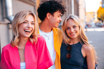 Group of young three stylish friends posing in the street. Fashion man and two cute female dressed in casual summer clothes. Smiling models having fun. Cheerful women and guy outdoors