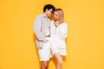 Happy beautiful romantic teenage couple. Smiling handsome caucasian man and young woman in summer clothes posing in studio, hugging sharing emotions, cheerful and happy. Isolated on yellow