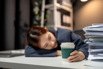 A woman is sleeping on a desk with a cup of coffee in front of her