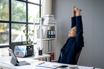 A man in a suit is stretching his arms and legs while sitting at a desk