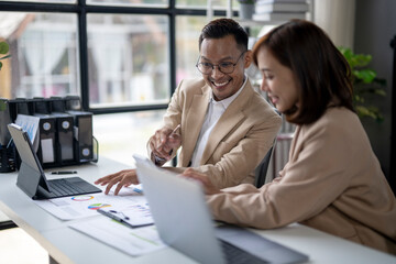 Two people are sitting at a desk with laptops and papers