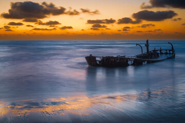 Wrecked fishing boat on the beach at sunset