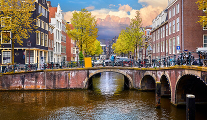 Obraz premium Netherlands Amsterdam. View at river Amstel with traditional houses bank and boats water canal. Scenic amsterdam cityscape. Spring day blue evening sky dramatic clouds.