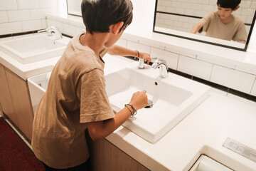 Asian boy washing his hands in front of a mirror after using public rest room at mall