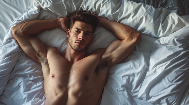 A man with a muscular body is laying on a bed with his arms crossed