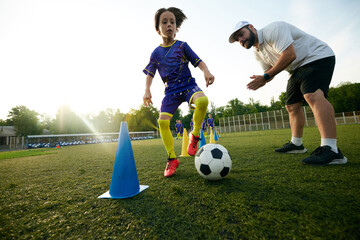 Male sport coach guiding young player through dribbling drill, encouraging and commentating. Focus and concentration. Concept of sport, childhood, education, achievement, active lifestyle