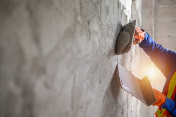 Close-up of plastering worker's hands wearing orange rubber gloves.