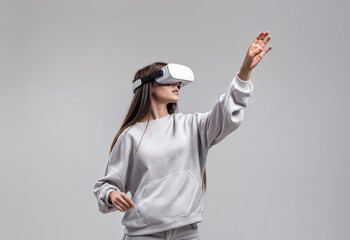 A young woman in a grey sweatshirt, wearing virtual reality goggles and holding her arm up.