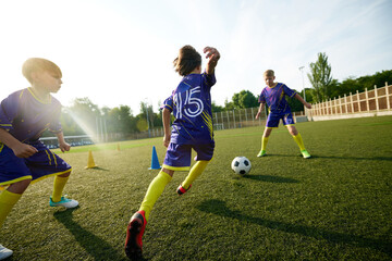 Little active boys, children in sportswear training on outdoor stadium on sunny day, growing soccer skills and team spirit. Concept of sport, childhood, education, achievement, active lifestyle
