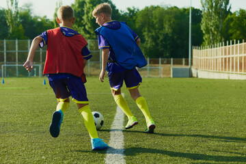 Young players improve their techniques, children in red and blue uniforms, soccer players in motion on outdoor stadium training. Concept of sport, childhood, education, achievement, active lifestyle