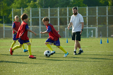 Obraz premium Boys, children in red and blue uniforms in motion on outdoor stadium, competing for victory, training soccer game. Concept of sport, childhood, education, achievement, active lifestyle