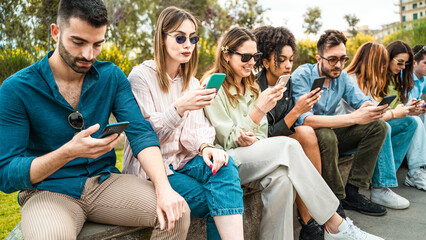 Diverse group of young people using smartphones outdoors in park, social media addiction and technology concept