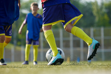 Naklejka premium Focused on legs in sportswear, soccer players in motion with ball on field, playing, dribbling ball. Sport school. Concept of sport, childhood, education, achievement, active lifestyle