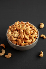 Roasted Organic Cashews in a Bowl on a black background, side view.