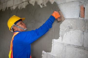 Asian builder plastering walls at construction site