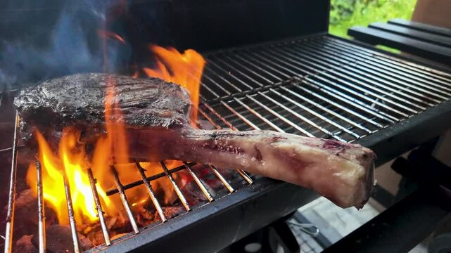 Tomahawk steak on the grill with fire flames in slow motion.