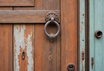Fototapeta premium A weathered wooden door with a rusty knocker and peeling paint. 