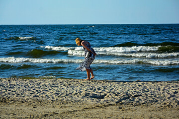 dziewczyna w kapeluszu na plaży szukajaca muszelek, schylona dziewczyna na tle morza, a girl in a hat on the beach looking for shells, a girl bending over against the background of the sea, © kateej