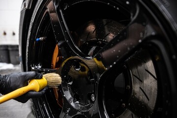 Detailing car wheel using brush for thorough cleaning. Focus on precision and high-quality finish in professional auto detailing, ensuring spotless and shiny wheels