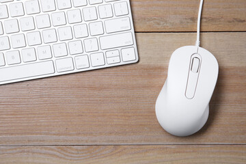 Wired mouse and computer keyboard on wooden table, flat lay. Space for text