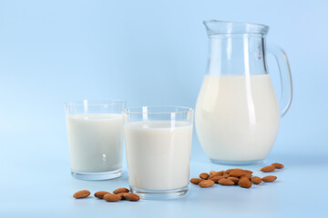 Fresh almond milk in glasses, jug and nuts on light blue background
