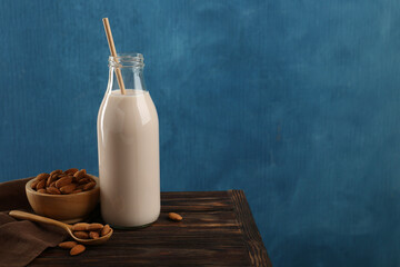 Fresh almond milk in glass bottle, nuts and spoon on wooden table, space for text