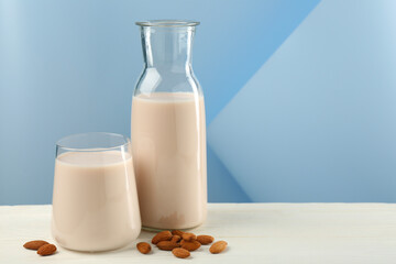 Fresh almond milk in carafe, glass and nuts on white wooden table, space for text