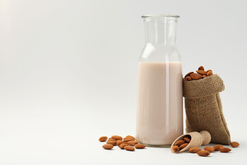Fresh almond milk in carafe, nuts, scoop and burlap sack on white background, space for text