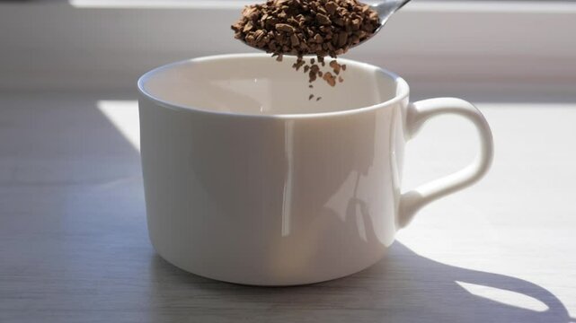 Pour instant coffee into a coffee cup in slow motion. Sprinkle instant coffee beans with a spoon