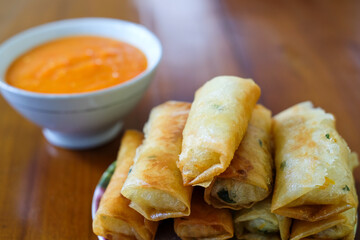 Fried spring rolls on white plate, served with chili sauce sambal on top the wood table, traditional snack, Traditional spring rolls, copy space .