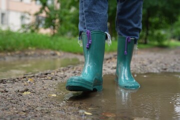 Woman wearing turquoise rubber boots walking in puddle outdoors, closeup. Space for text