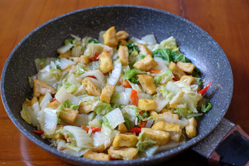 Stir fry tofu and chinese cabbage in  the pan on a wood table, Indonesian dish eaten with rice.